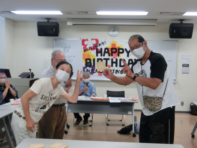 ピースしている男女のメンバー2名の写真。男性がプレゼントを貰って、喜んでいる。2人ともにこやかに笑っている。