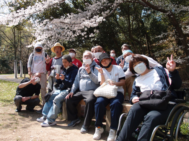 桜を背景に集合写真。みんなピースをしてにこやかに笑っている。