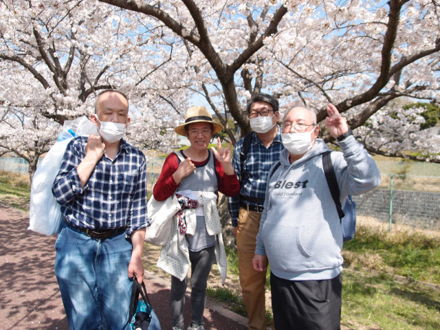 4名の男性メンバーの写真。桜を背景にしている。