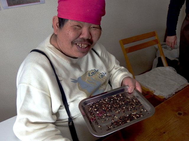 今、選別中の古代米を片手に持つ男性の写真。カメラ目線で満面の笑み。