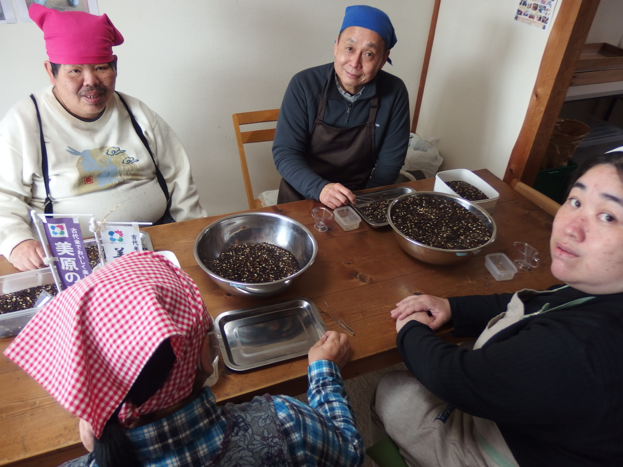 美原区の特産品である古代米を選別している写真。小石といった不純物を取り除いている。4名の男女が写っている。うち1名スタッフ。他メンバー。