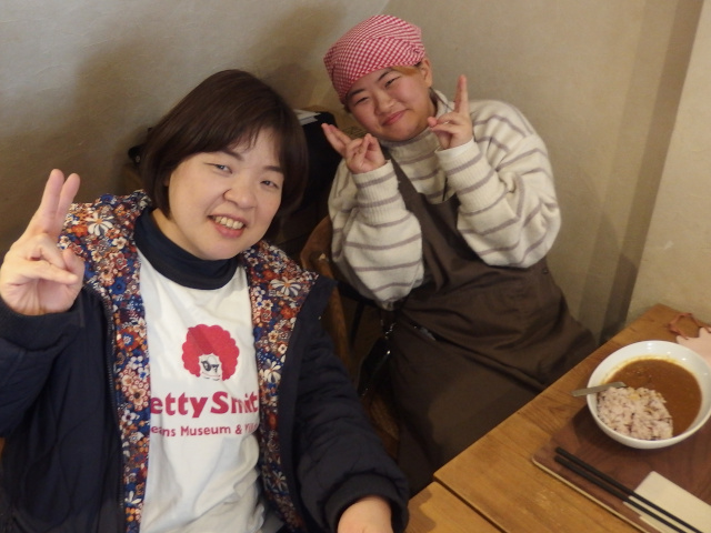 ピースしている女性2名。スタッフとメンバー。メンバーは休憩中。三角巾とエプロンを付けている。