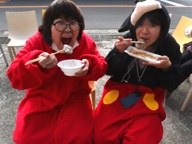 椅子に座って餅を食べている女性2名。カメラ目線で、今まさに食べるぞ！という感じで餅を口元に持っていき、アピールしている。