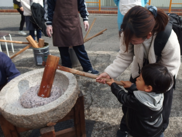 3歳ほどの小さい子供と、そのお母さんの写真。親子で一緒に同じ杵を持ちながら餅つきしている。