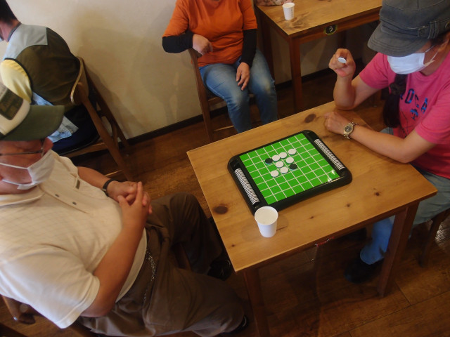 オセロをしている写真。貸切中のカフェに複数のメンバーが居る。中心に写っている男女がオセロで対戦をしている。ゲームは始まったばかりでまだコマはあまり置かれていない。