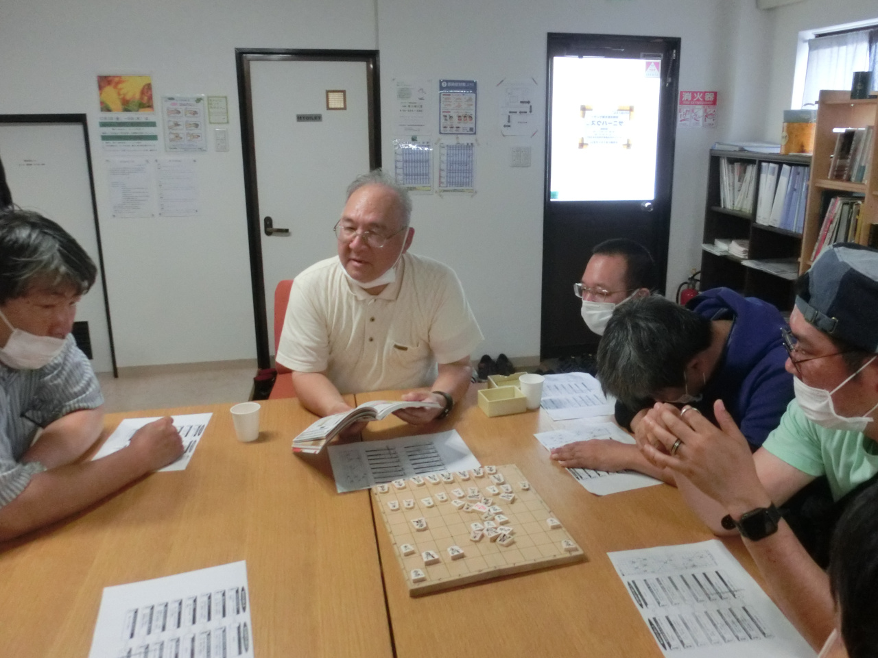 5名の男性メンバー。指導者の男性が講義している。